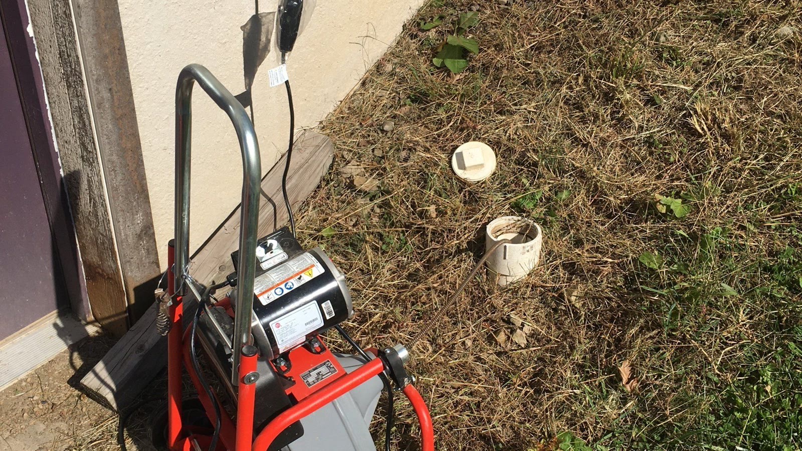 Drain-cleaning machine positioned beside an exterior residential cleanout